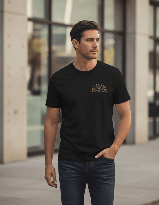 Male model wearing a black Supima cotton Lilak T-shirt featuring a gold mandala-inspired chest graphic, walking outdoors in an urban setting with modern glass buildings in the background