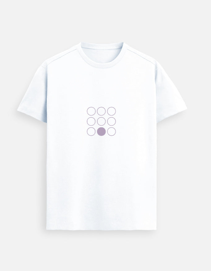 Indian female model wearing a White Supima cotton T-shirt by Lilak, featuring a minimal lavender geometric circle design on the center chest. She stands in a softly lit studio with large window shadows in the background