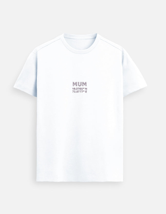 Male model wearing a White Supima cotton T-shirt by Lilak with ‘MUM’ and Mumbai coordinates printed on the center chest, standing in a modern softly lit studio environment