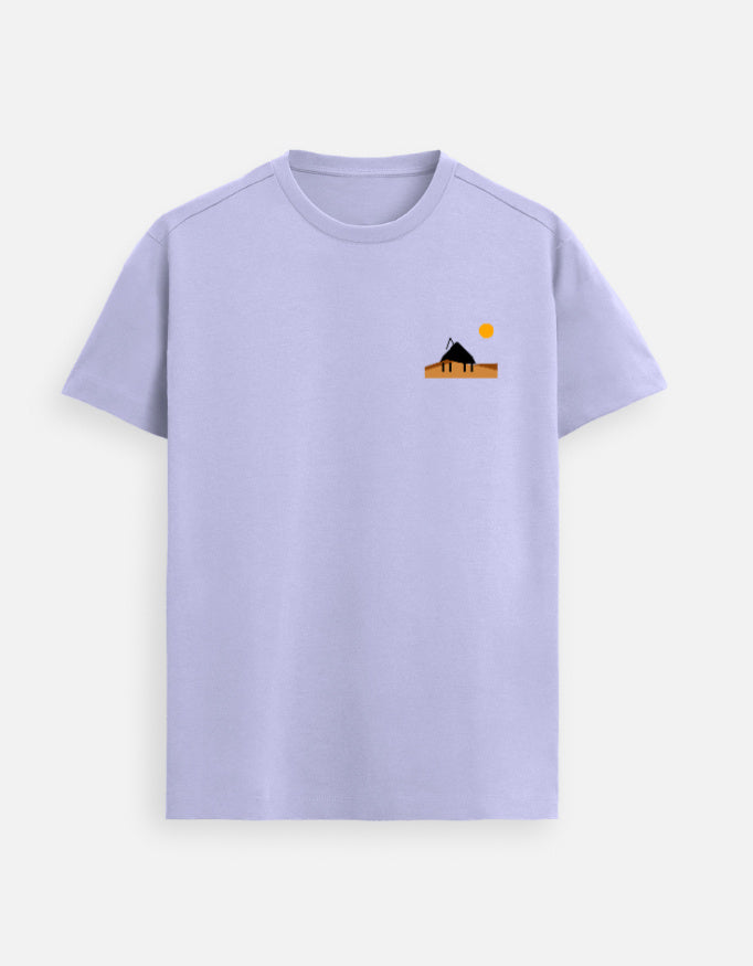 Male model standing in a softly lit studio wearing a Lavender Supima cotton T-shirt by Lilak, featuring a minimal sunset hut graphic on the left chest