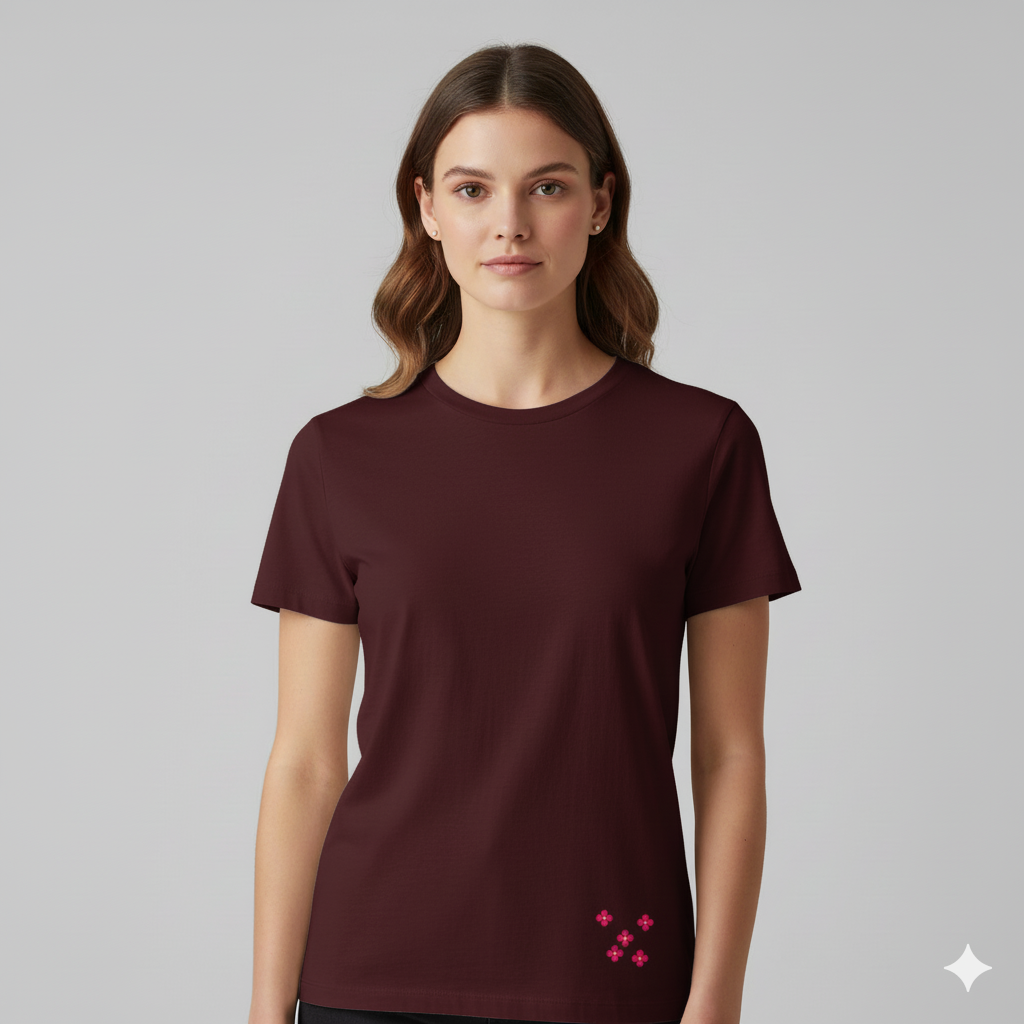Female model wearing a MaroonSupima cotton T-shirt by Lilak, featuring a small pink floral cluster printed near the bottom left hem, photographed against a plain light grey studio background
