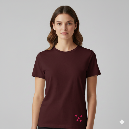 Female model wearing a MaroonSupima cotton T-shirt by Lilak, featuring a small pink floral cluster printed near the bottom left hem, photographed against a plain light grey studio background