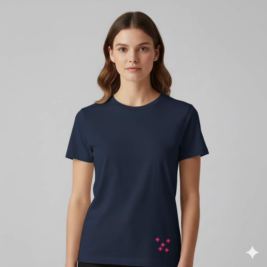 Female model wearing a Navy Blue Supima cotton T-shirt by Lilak, featuring a small pink floral cluster printed near the bottom left hem, photographed against a plain light grey studio background